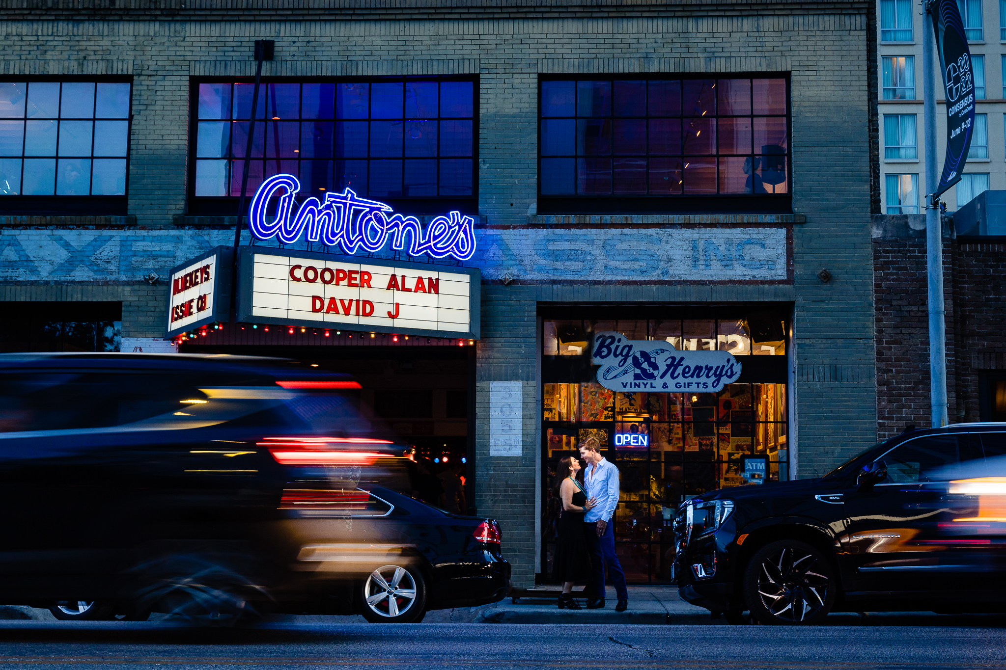 Couple stands on street outside Antone's night club in the evening while cars pass by in front of the camera