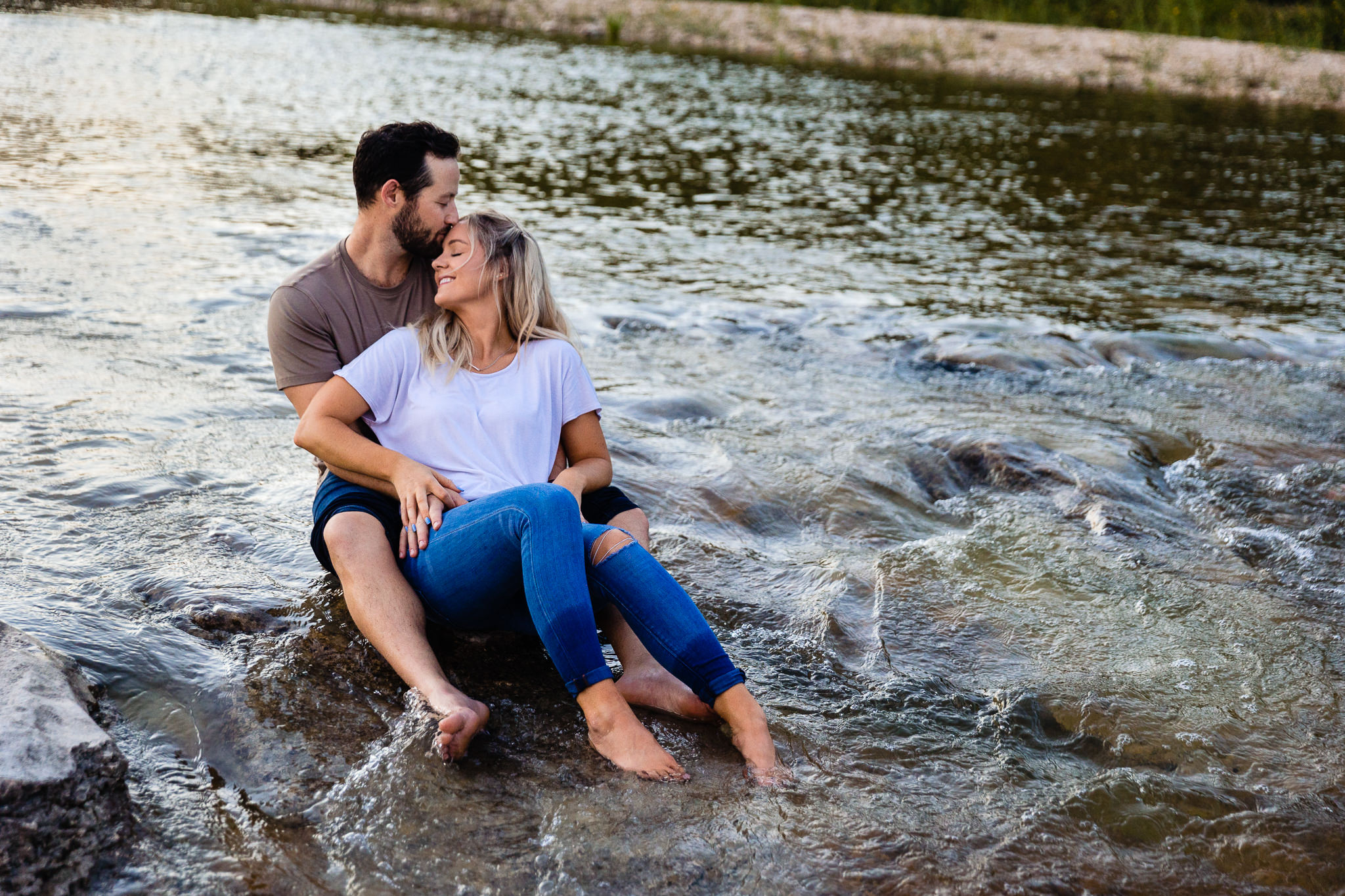 Future bride sits in future husbands lap while seated on a rock in the middle of a flowing stream