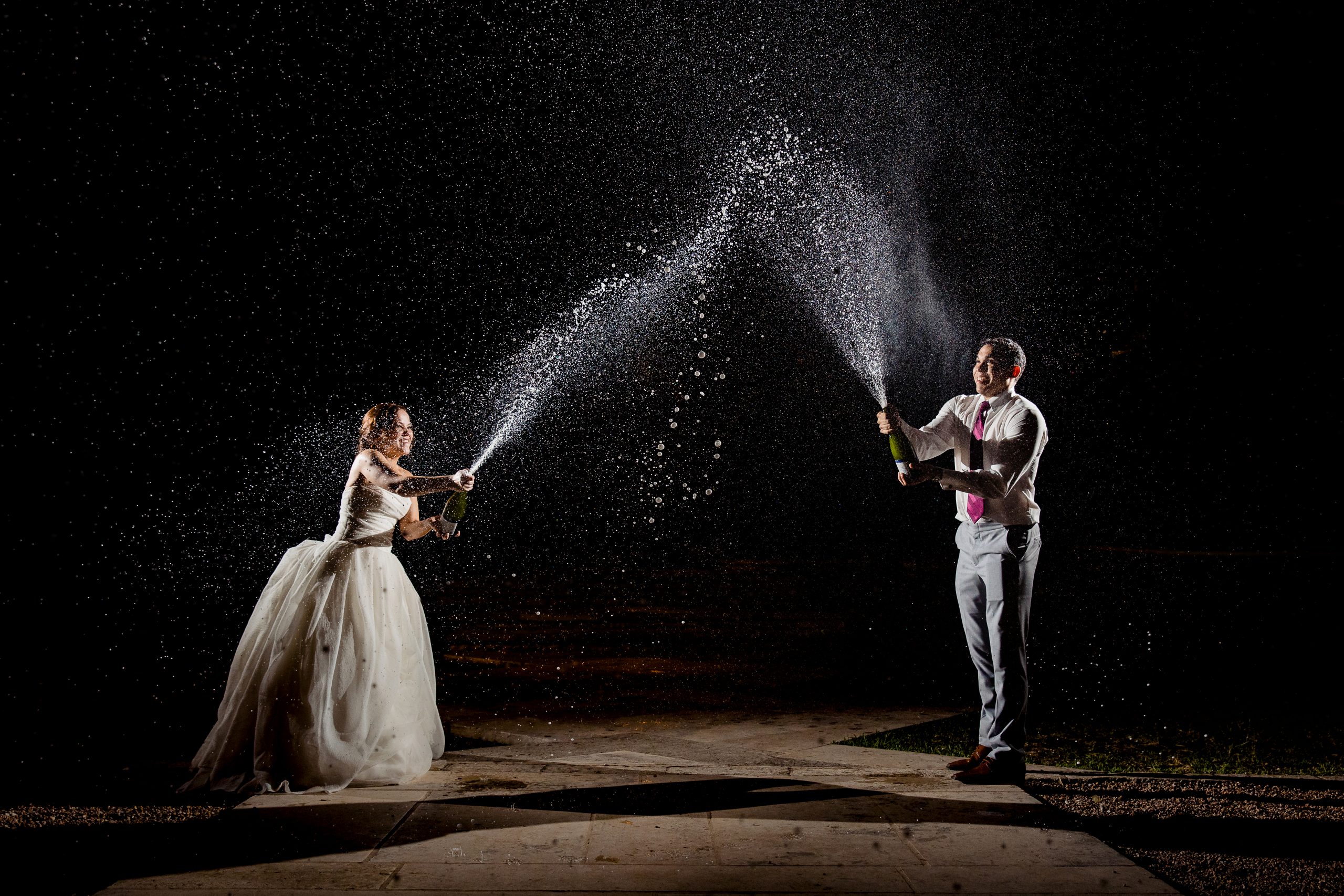 Couple at night on wedding day sprays champagne at each other while laughing with joy